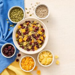 A hand-mixed bowl of seeds and dried fruit with single-ingredient bowls around it